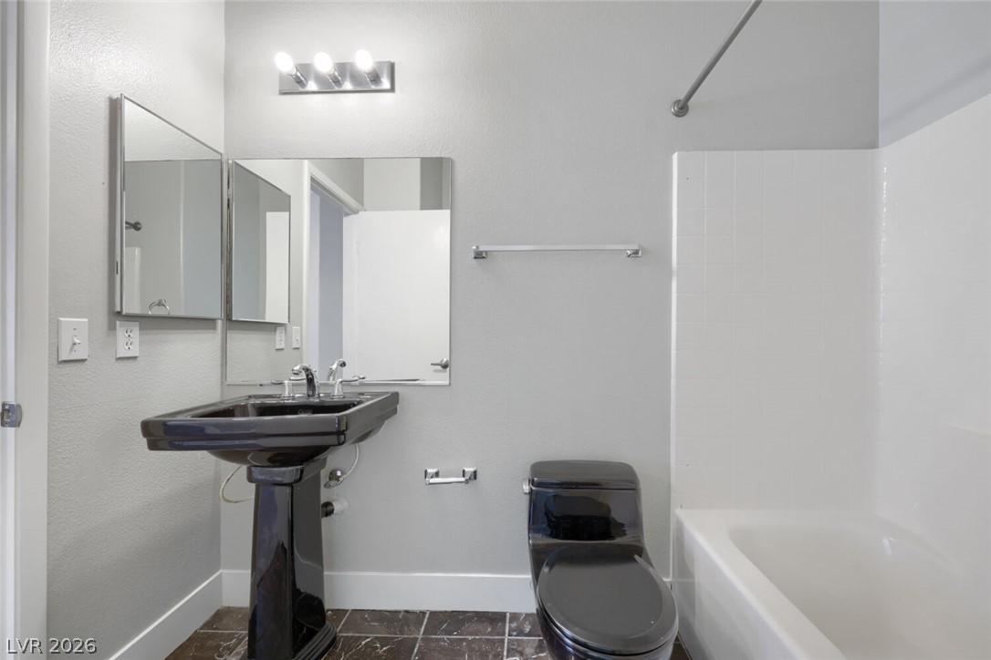 5985 High Steed Street, Unit 101 Henderson, NV 89011 - Photo 29 of 38 A well-lit bathroom features a striking black pedestal sink and toilet, complemented by a white bathtub.
