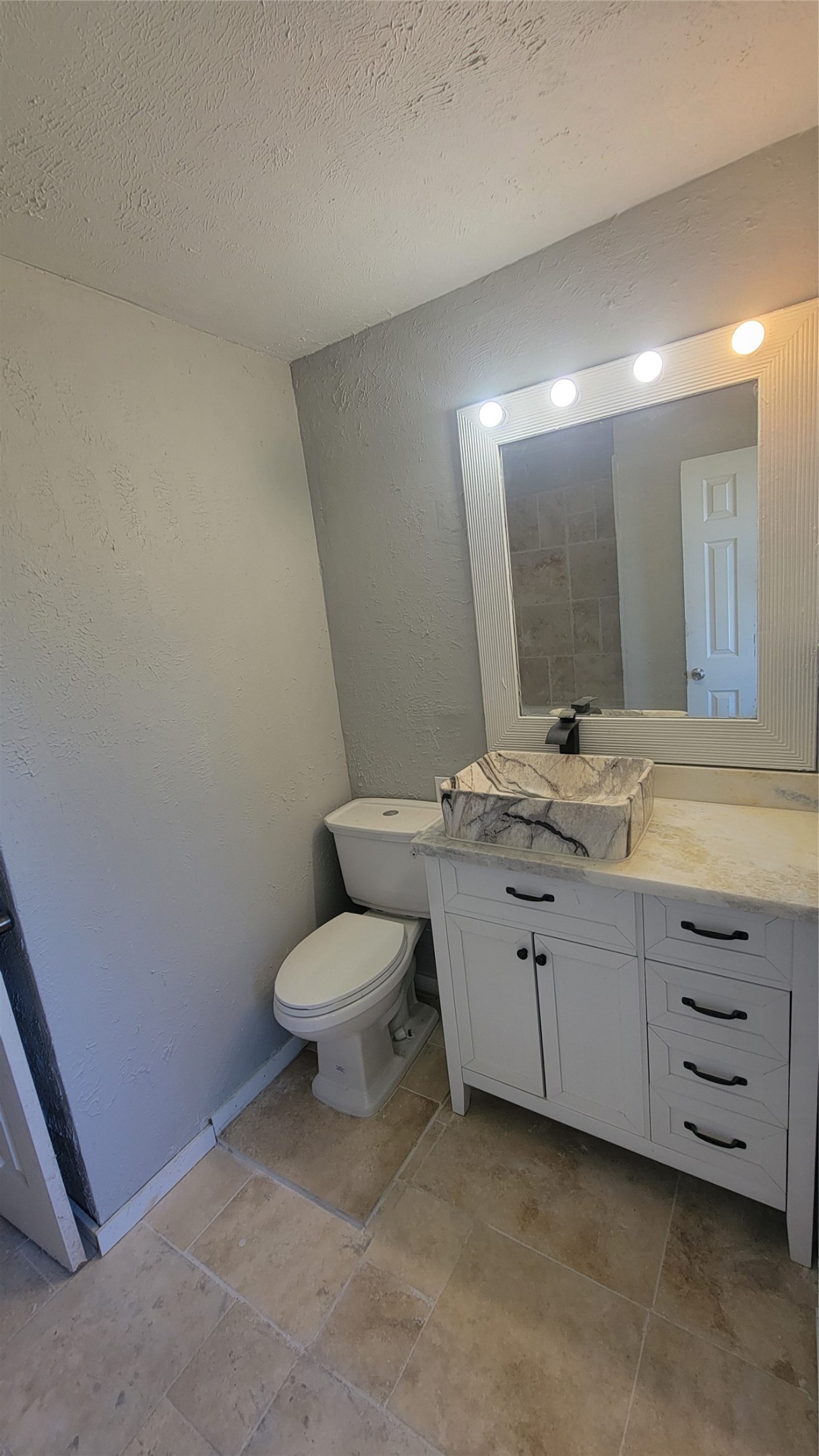 12018 Sandpiper Road Angleton, TX 77515 - Photo 14 of 48 This bathroom features a modern design with a white vanity and marble vessel sink. It has a large, lighted mirror and neutral tile flooring, creating a clean and bright space.