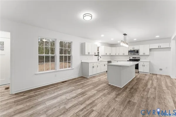 a large white kitchen with kitchen island a stove a sink dishwasher and white cabinets with wooden floor