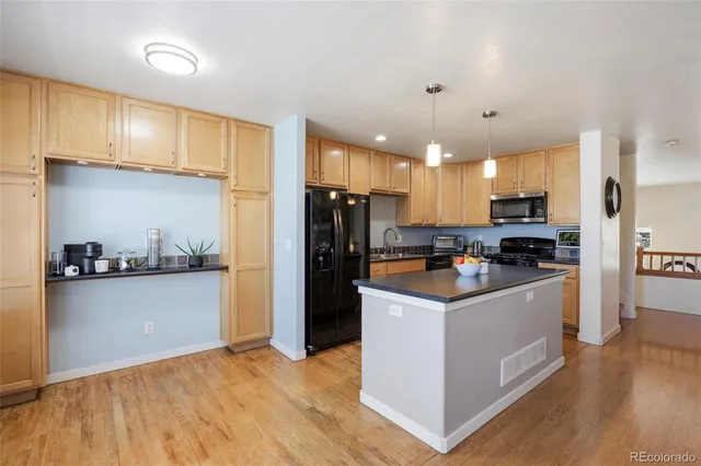 a kitchen with stainless steel appliances a stove top oven a refrigerator a sink dishwasher and a dining table with wooden floor