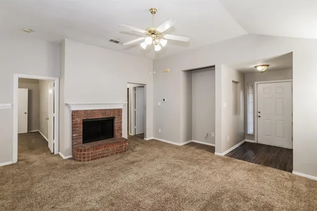 a view of an empty room with chandelier fan and fire place