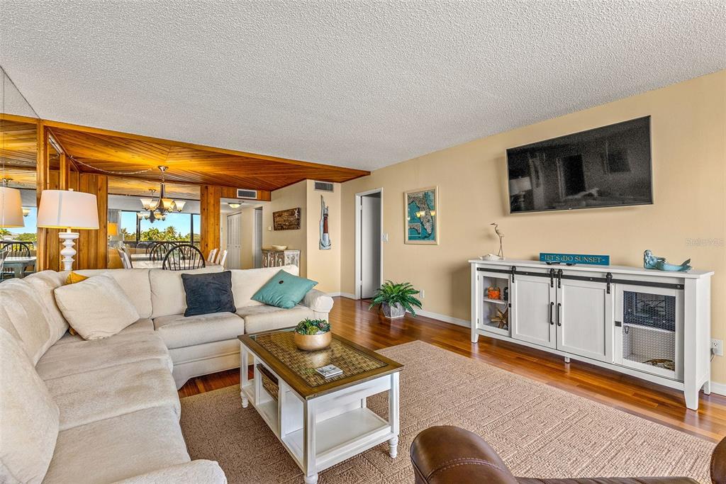 9495 Blind Pass Road, Unit 202 St. Pete Beach, FL 33706 - Photo 17 of 55 a living room with furniture a flat screen tv and a floor to ceiling window