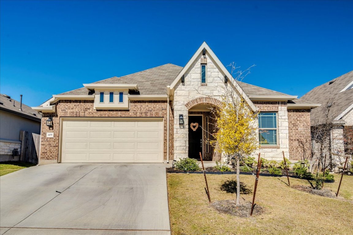French country home with brick siding, driveway, a front lawn, stone siding, and an attached garage
