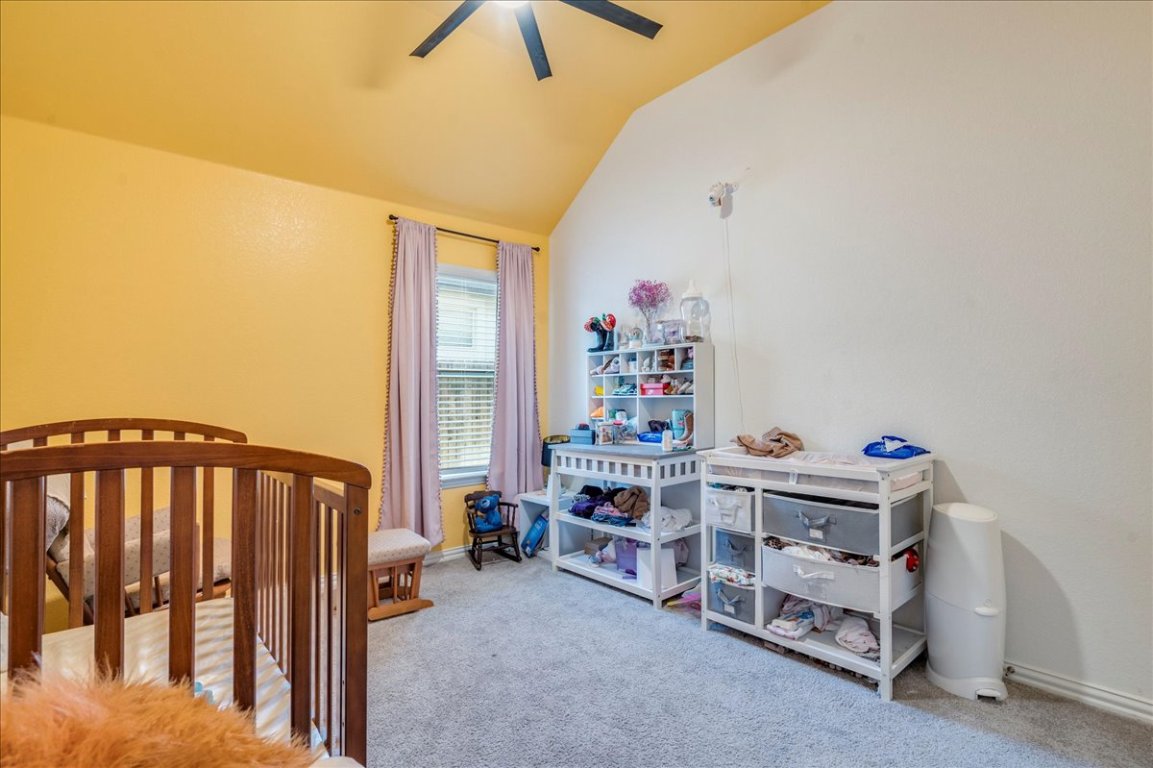 409 Durian Loop Buda, TX 78610 - Photo 16 of 30 Bedroom featuring a crib, light colored carpet, lofted ceiling, and a ceiling fan