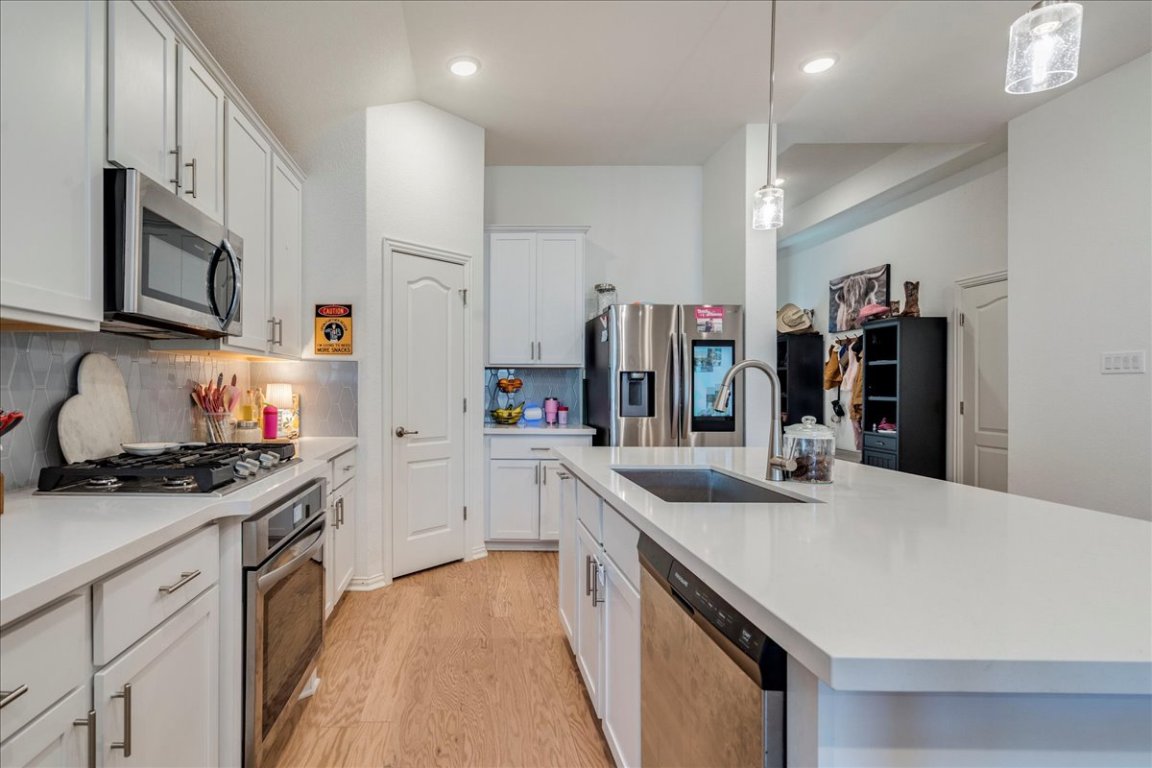 409 Durian Loop Buda, TX 78610 - Photo 6 of 30 Kitchen with appliances with stainless steel finishes, hanging light fixtures, white cabinets, light wood-type flooring, and decorative backsplash