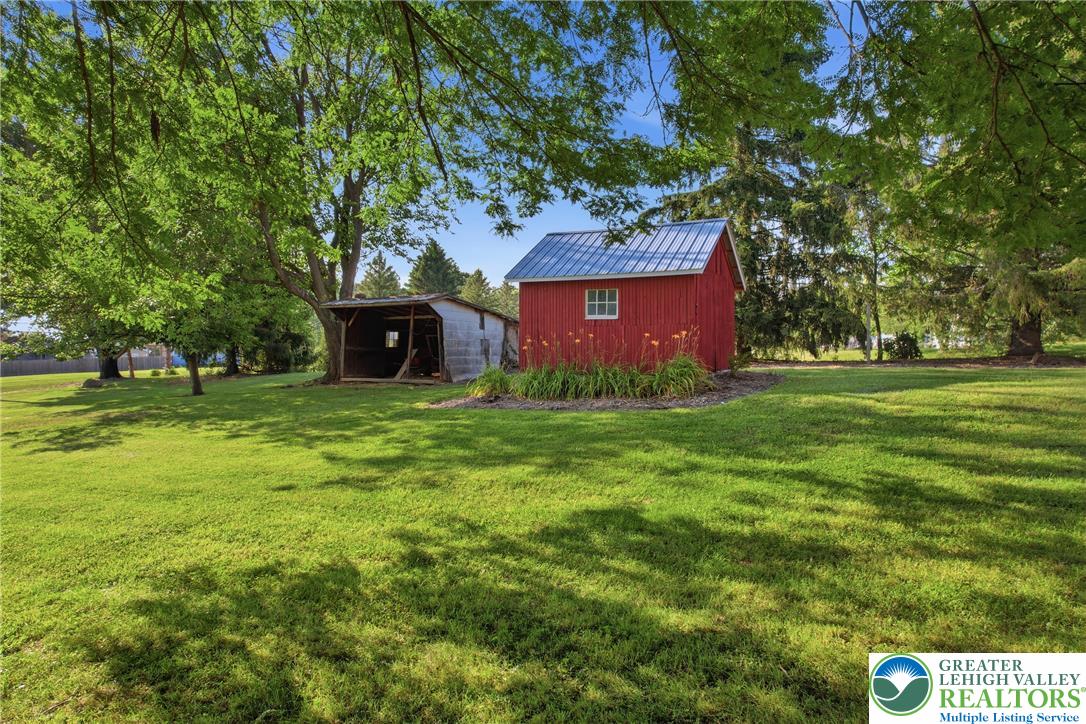 4682 Steuben Road Bethlehem, PA 18020 - Photo 62 of 79 A spacious backyard features a vibrant red shed and a covered outbuilding amidst lush greenery.