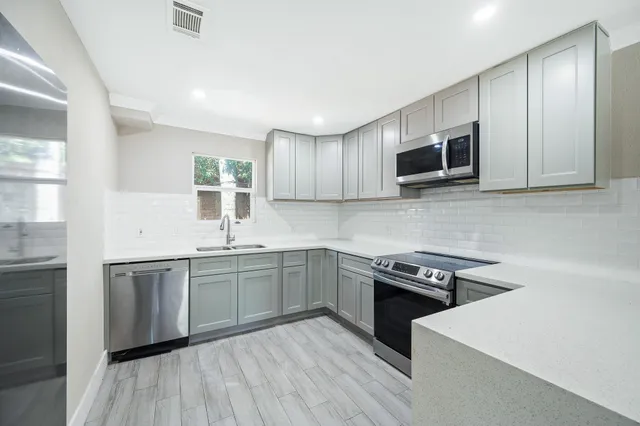 a kitchen with stainless steel appliances a sink dishwasher a stove top oven a refrigerator with grey cabinets and wooden floor