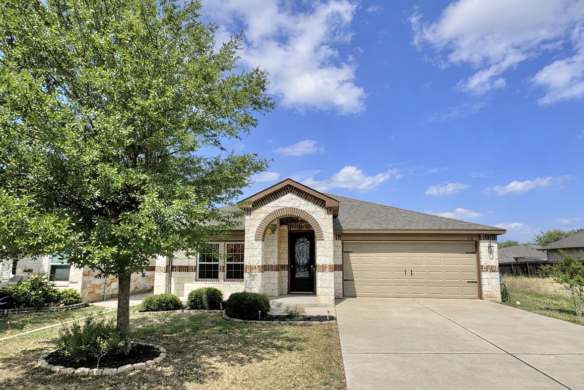 Home featuring stone siding, an attached garage, concrete driveway, brick siding, and a front yard