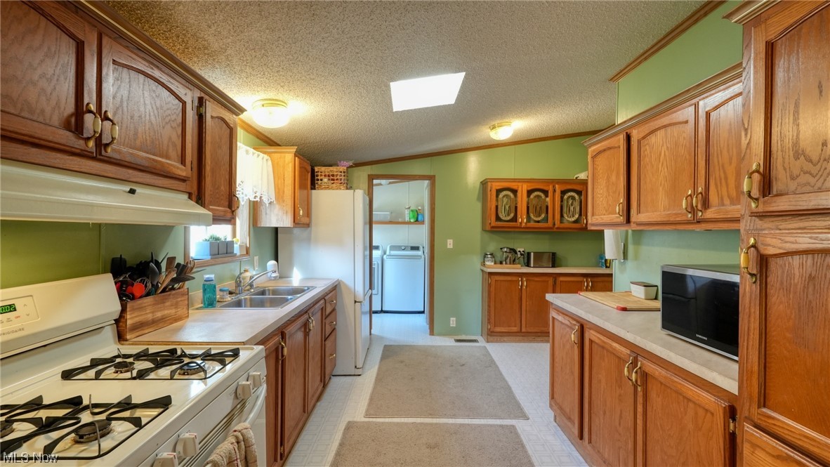 53447 Mud Run Road Senecaville, OH 43780 - Photo 7 of 31 Kitchen featuring washer / dryer, sink, a textured ceiling, white appliances, and vaulted ceiling with skylight