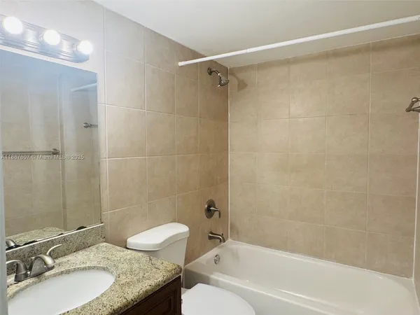 a bathroom with a granite countertop bathtub shower sink vanity and a toilet