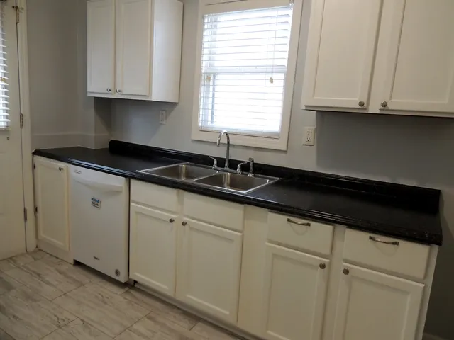 a kitchen with granite countertop white cabinets sink and window