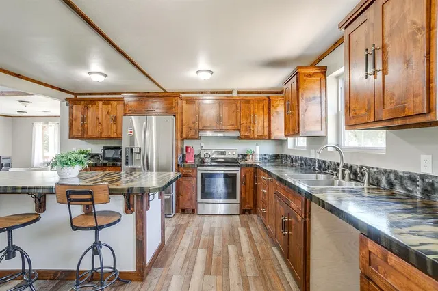 a kitchen with stainless steel appliances granite countertop wooden cabinets a sink dishwasher a stove and a refrigerator with wooden floor