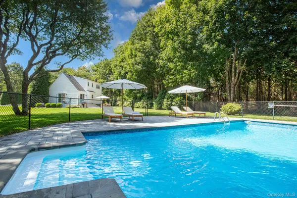 a view of swimming pool with lawn chairs and large trees