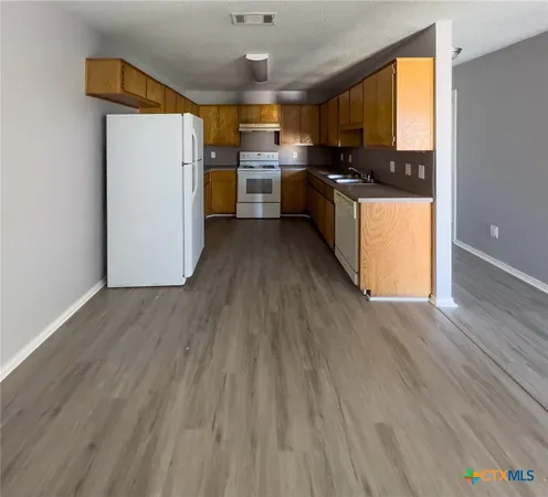 a kitchen with a refrigerator a stove top oven a chimney wooden floor and cabinets