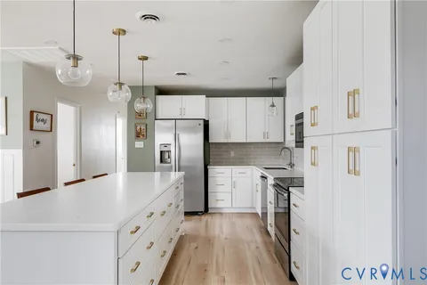 a large kitchen with stainless steel appliances a refrigerator a sink dishwasher a oven and white cabinets with wooden floor