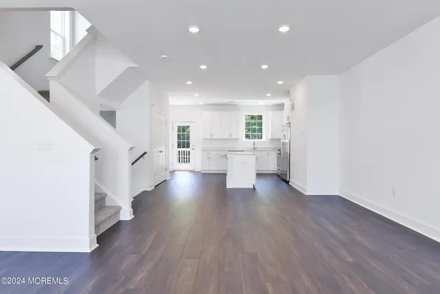 a view of an empty room and a kitchen with wooden floor