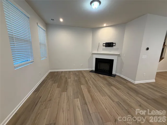 an empty room with wooden floor fireplace and windows