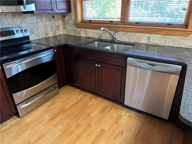 a kitchen with stainless steel appliances granite countertop a refrigerator a sink a stove a microwave and wooden floors