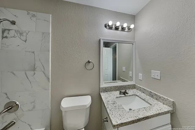 a bathroom with a granite countertop sink a toilet and mirror