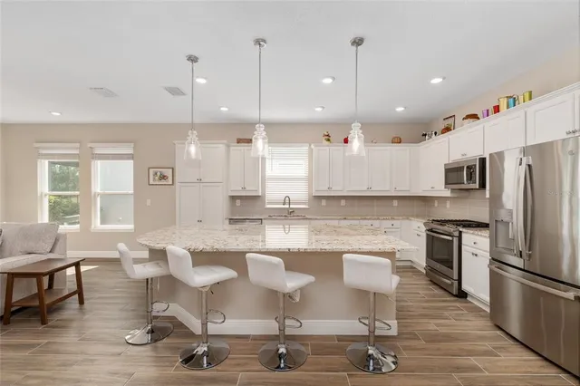 a large kitchen with kitchen island a large island a stove a chandelier and living room view