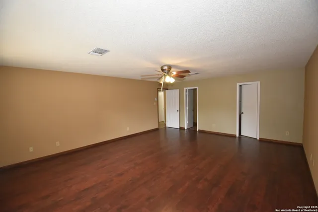 a view of an empty room with wooden floor and a ceiling fan