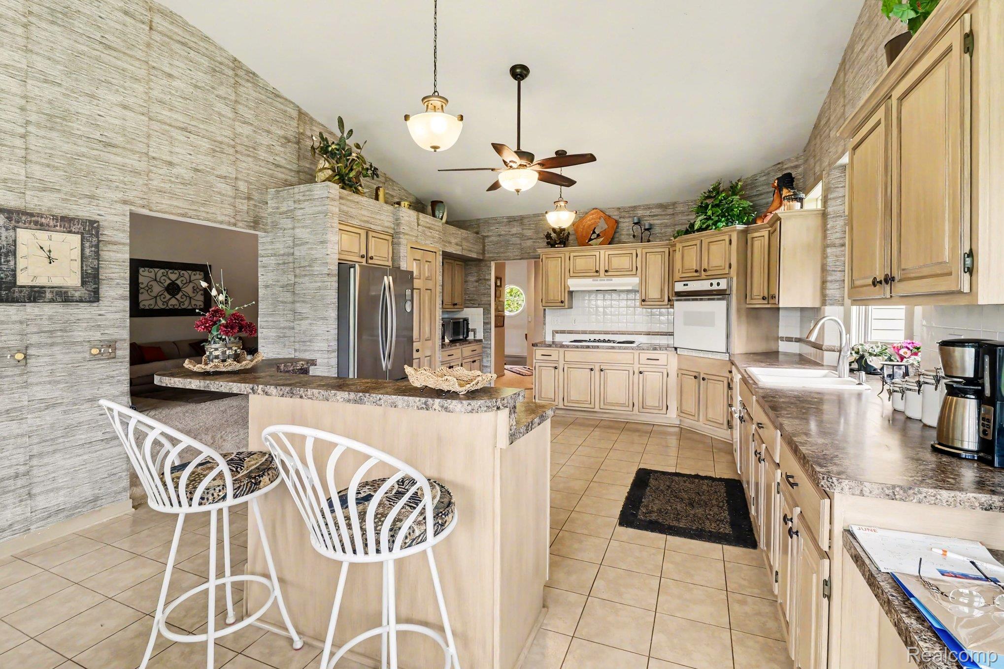 18501 Taylor Lake Road Holly, MI 48442 - Photo 14 of 35 Spacious kitchen featuring tile flooring, light wood-finish cabinetry, built-in appliances, a breakfast bar, and vaulted ceilings with ceiling fans