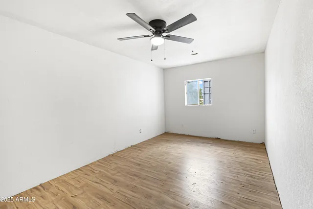 an empty room with wooden floor chandelier fan and windows