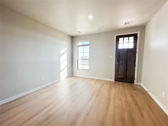 a view of an empty room with wooden floor and window