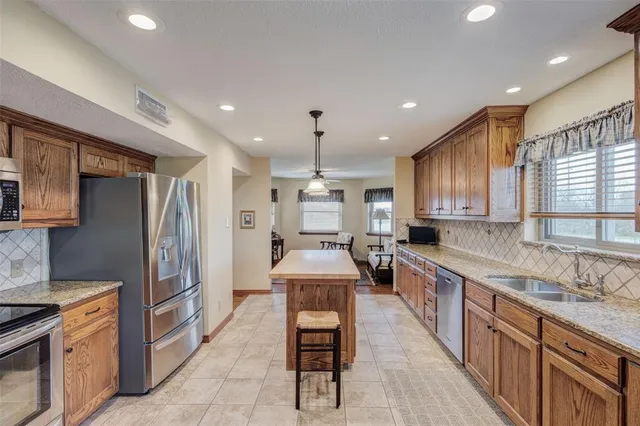 a large kitchen with stainless steel appliances kitchen island granite countertop a sink and a refrigerator