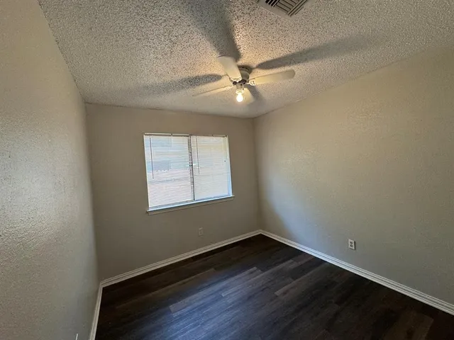an empty room with wooden floor fan and windows