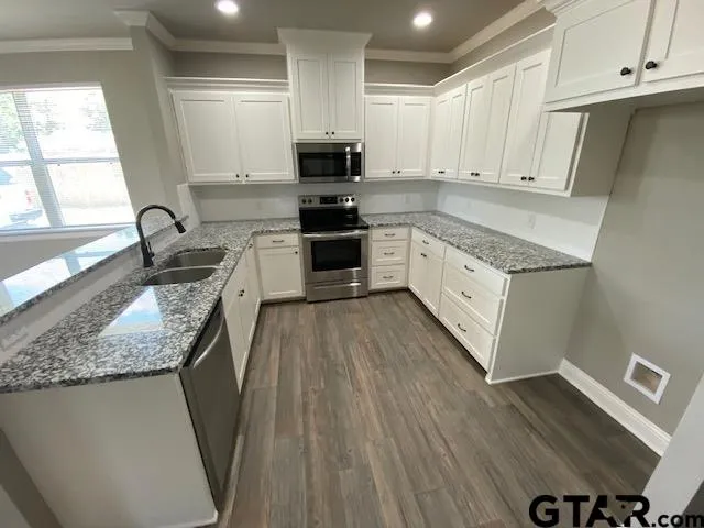 a kitchen with granite countertop a stove a sink dishwasher and a microwave oven with white cabinets