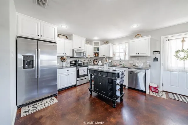 a kitchen with stainless steel appliances granite countertop a refrigerator a sink dishwasher a stove top oven a refrigerator and white cabinets with wooden floor