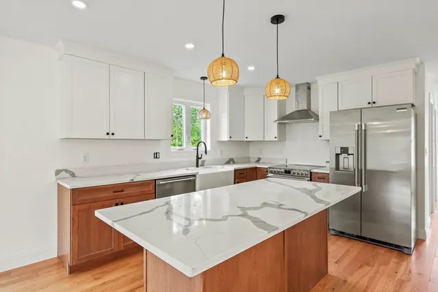 a kitchen with stainless steel appliances granite countertop a sink a refrigerator a stove a chimney a dining table and chairs with wooden floor