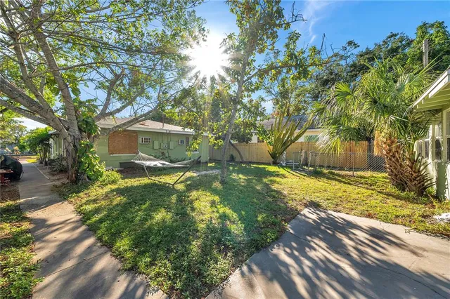 a backyard of a house with table and chairs plants and large tree