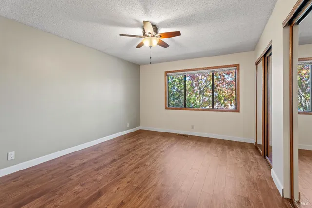 an empty room with wooden floor chandelier fan and windows