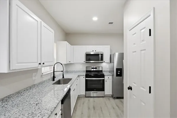 a kitchen with granite countertop a sink stainless steel appliances and white cabinets