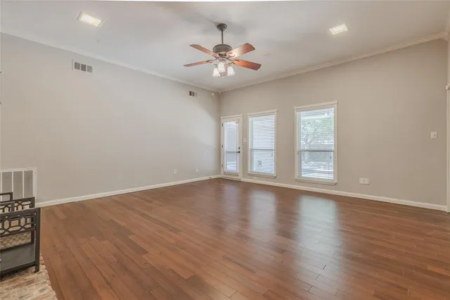 an empty room with wooden floor chandelier fan and windows