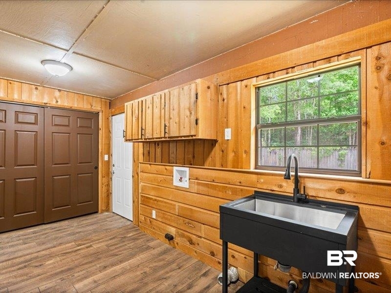 3160 Old Castleberry Road Brewton, AL 36426 - Photo 18 of 36 Utility room featuring wood-finish flooring, natural wood paneling, wood cabinetry, a stainless steel utility sink with a matte black faucet, and a large window