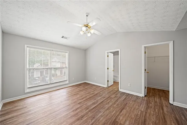 an empty room with wooden floor chandelier fan and windows