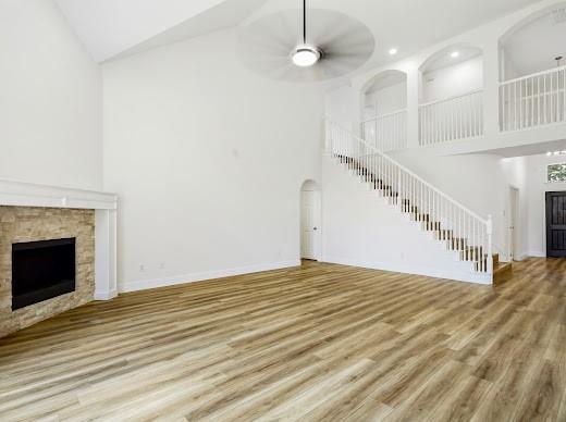 5034 West Fall Drive Midlothian, TX 76065 - Photo 13 of 40 Spacious living area featuring high vaulted ceilings, light wood-finish flooring, a stone-surround fireplace with white mantel, a white baluster staircase, and an overhead ceiling fan