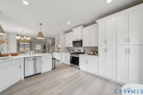 a large kitchen with cabinets a sink dishwasher a stove a refrigerator and white cabinets with wooden floor