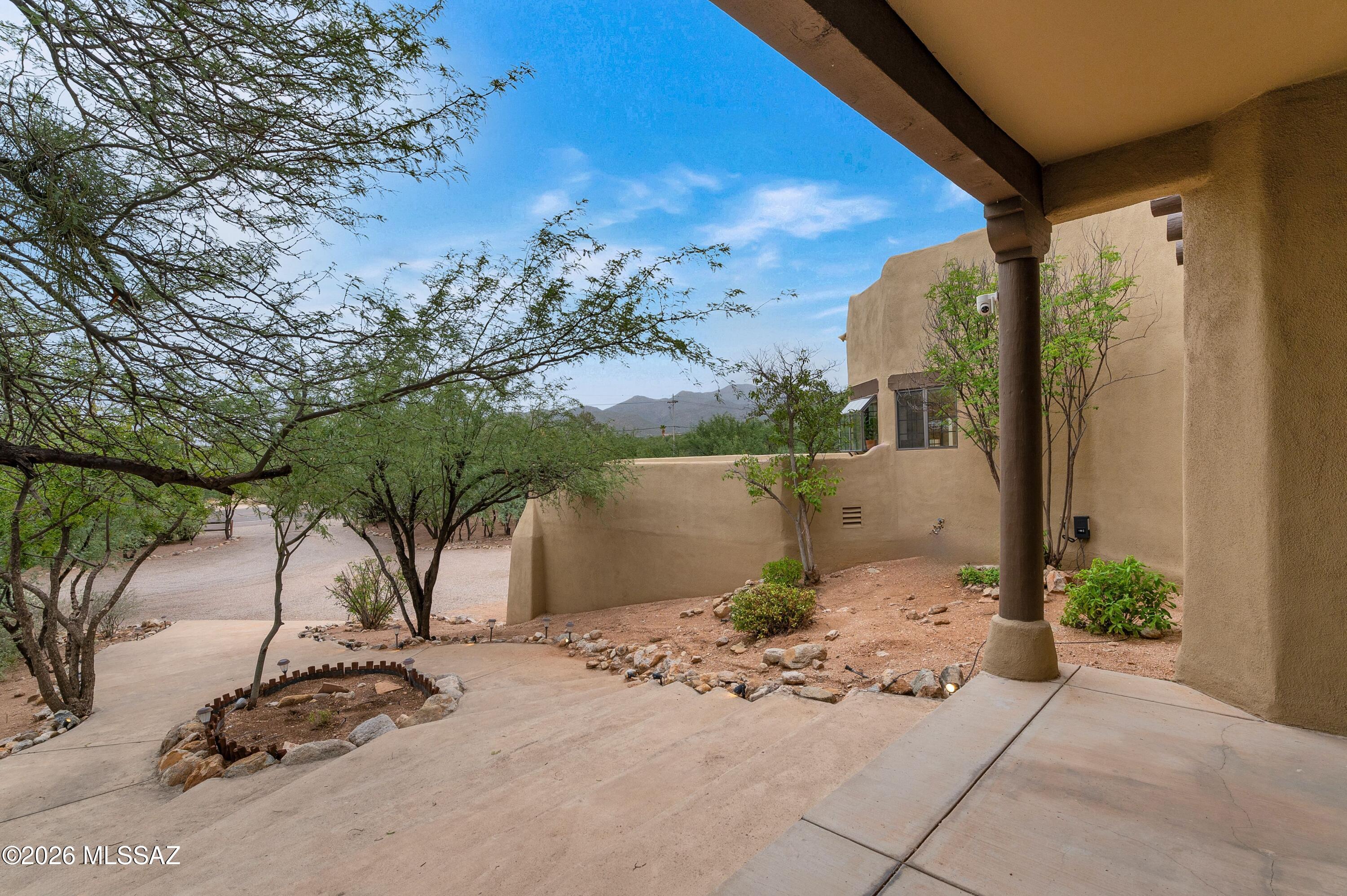12160 East Tanque Verde Road Tucson, AZ 85749 - Photo 22 of 53 Covered front portico with a stacked-stone fire feature, desert landscaping, and mountain views.