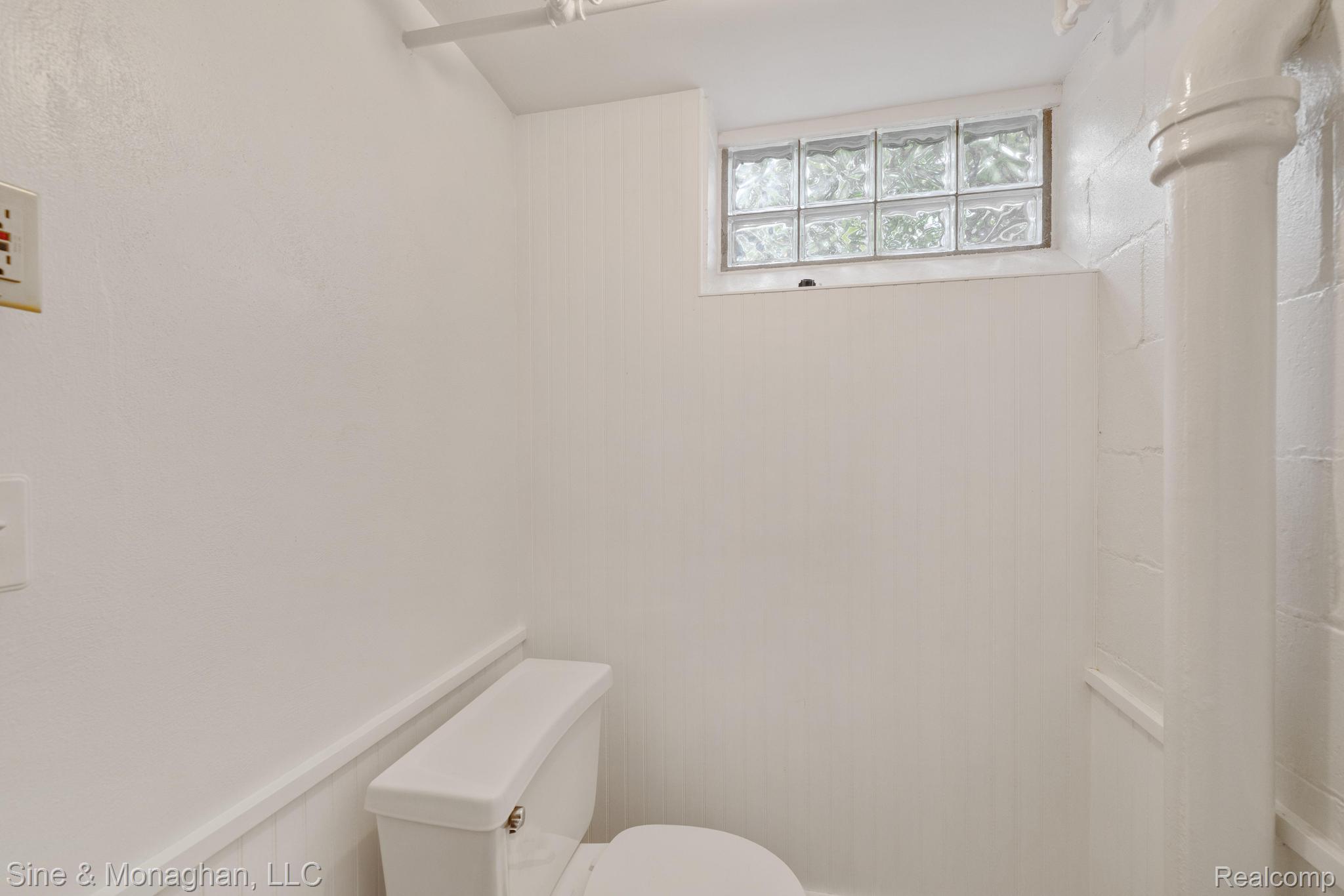 679 Neff Road Grosse Pointe, MI 48230 - Photo 36 of 78 White toilet, glass block window, beadboard wainscoting, painted concrete block wall, exposed painted ceiling pipe