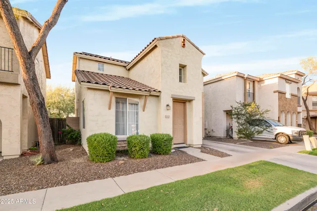 a view of a white house with a small yard and large tree and plants