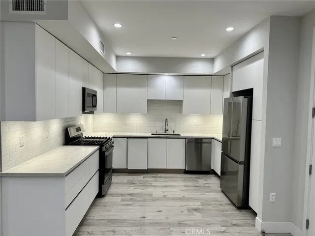 a large kitchen with stainless steel appliances granite countertop a stove a sink dishwasher and a refrigerator with wooden floor