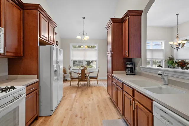 a kitchen with stainless steel appliances granite countertop a refrigerator a sink dishwasher a stove and a dining table with wooden floor