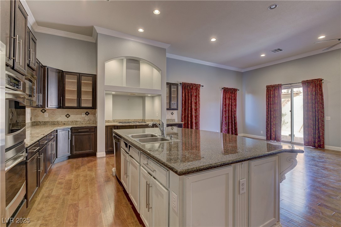 972 Rue Grand Paradis Lane Henderson, NV 89011 - Photo 5 of 32 Kitchen featuring crown molding, two tone cabinetry, a center island with sink, recessed lighting, and dark stone counters
