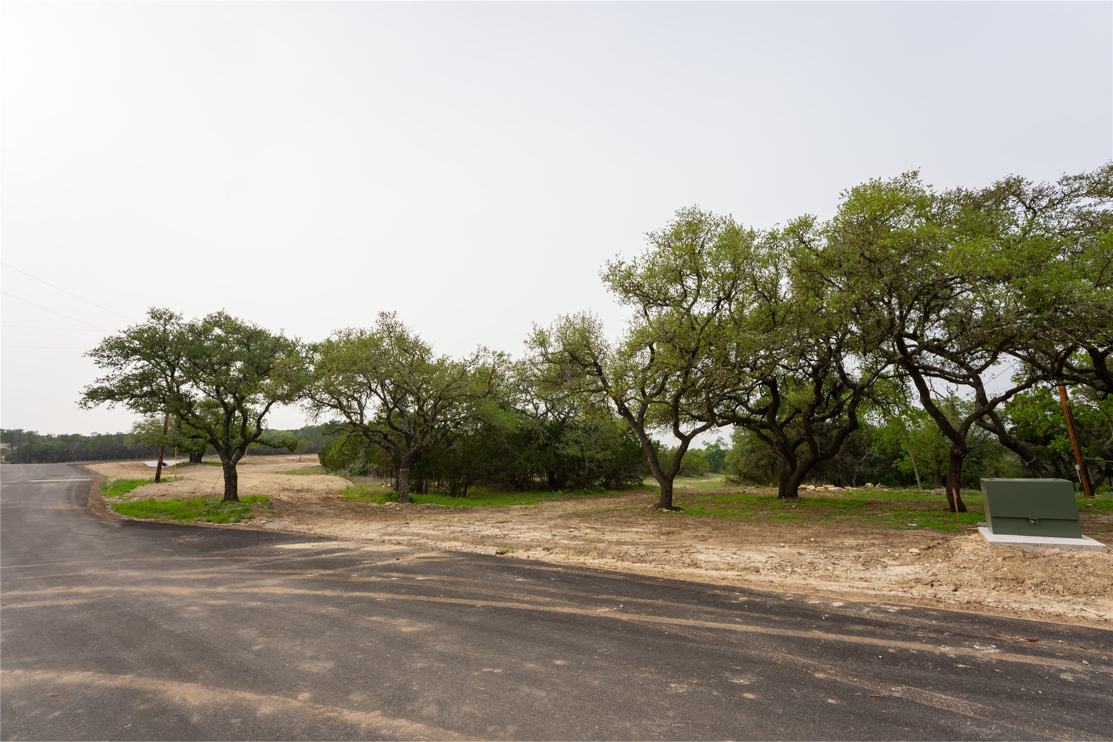 Lot 26 Ranch Road 165 Dripping Springs, TX 78620 - Photo 13 of 13 Paved road bordering a lot with mature trees, a utility box, and open land