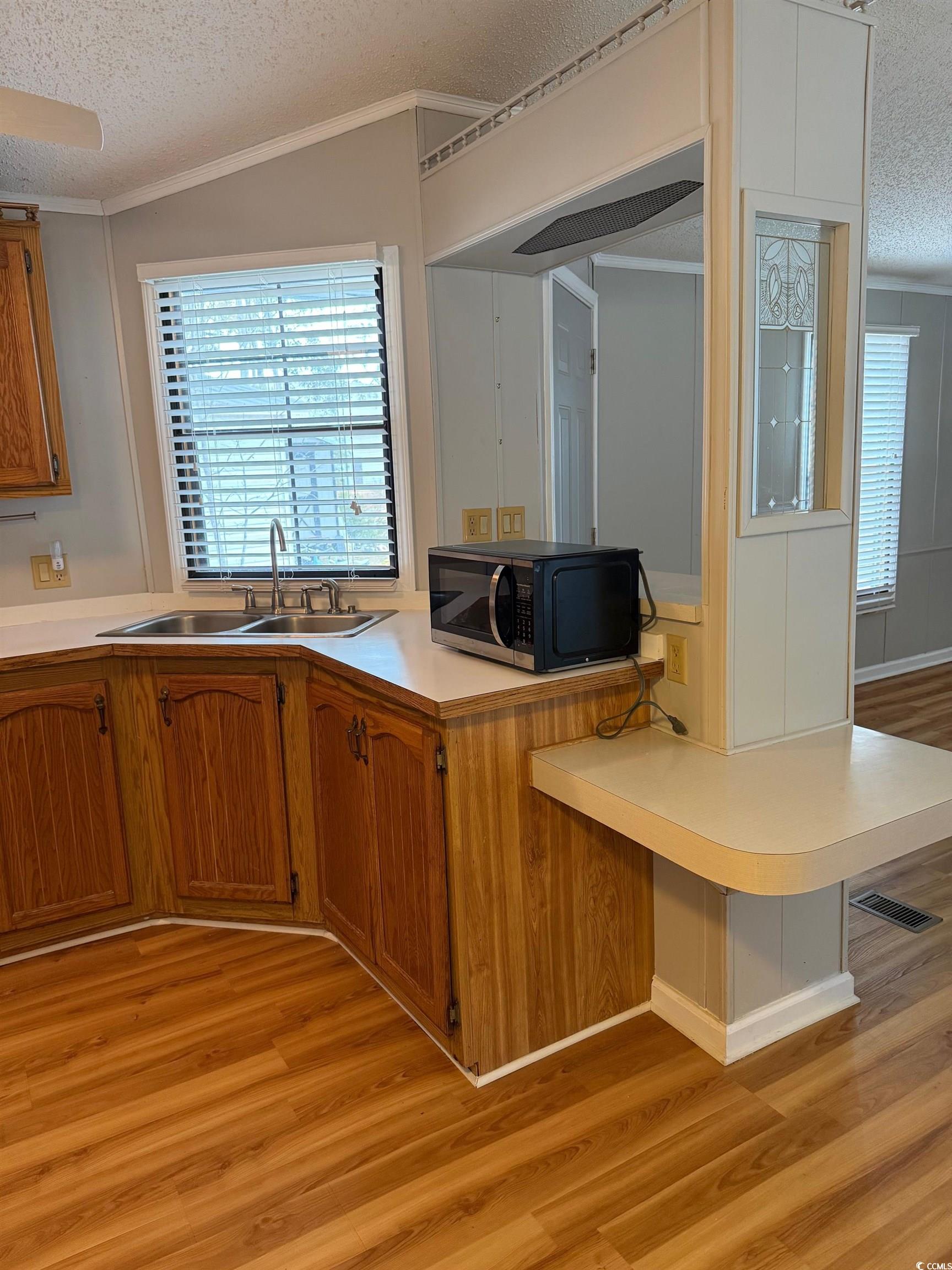 159 Crooked Island Circle Murrells Inlet, SC 29576 - Photo 6 of 20 Kitchen featuring a textured ceiling, light countertops, brown cabinets, light wood-style floors, and black microwave