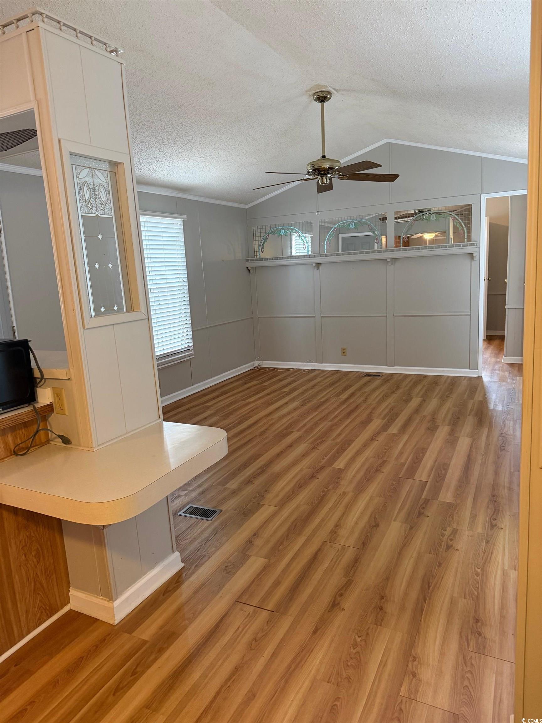 159 Crooked Island Circle Murrells Inlet, SC 29576 - Photo 8 of 20 Unfurnished living room with light wood-style floors, vaulted ceiling, a ceiling fan, a textured ceiling, and a decorative wall